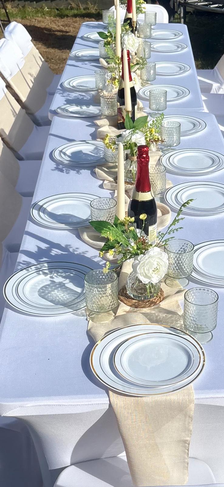 Long outdoor table set with gold-rimmed plates, taper candles and white florals